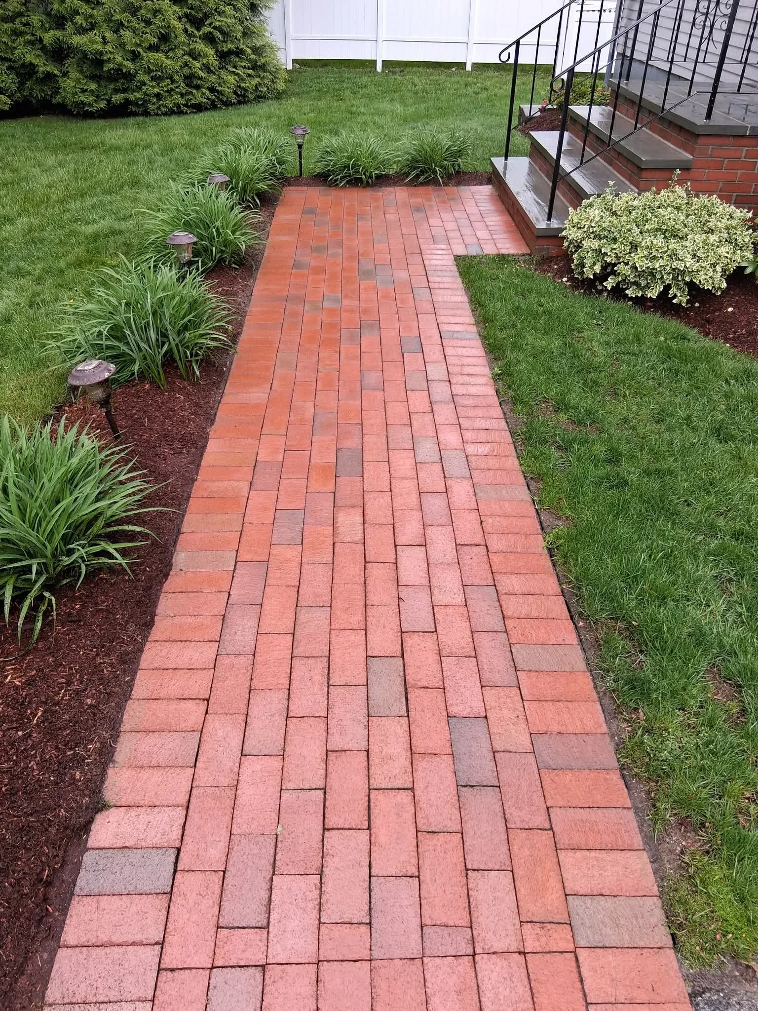 Clean red brick paver walkway with herringbone pattern, flanked by green lawn and landscaped beds