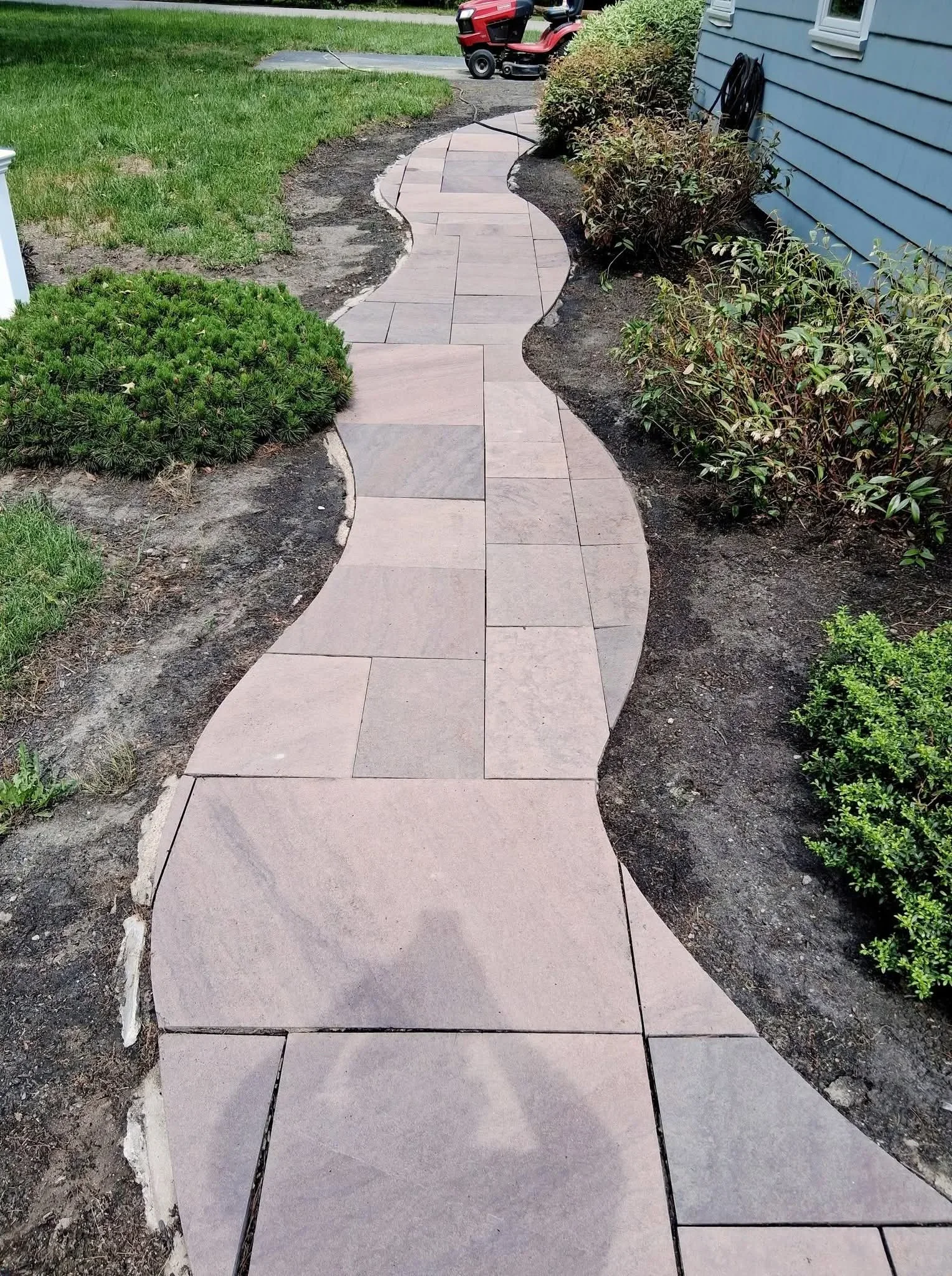 Curved paver walkway with taupe-colored stones and mulched landscape beds bordered by shrubs