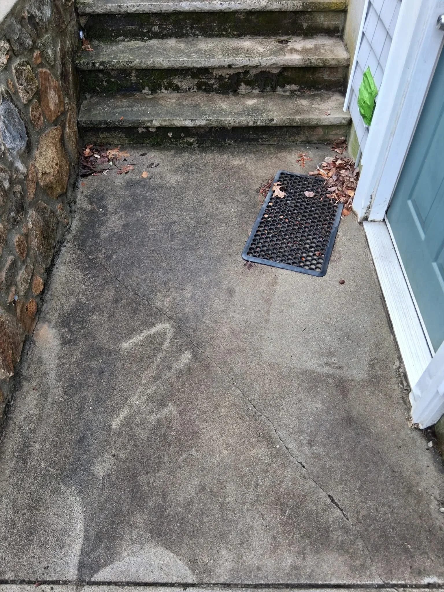 Concrete entryway stairs and landing after pressure washing, with stone wall and white door frame